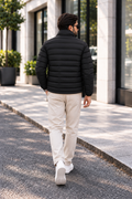 Man wearing horizontal quilted black winter puffer jacket street style walking back view