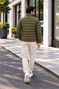 Man wearing horizontal quilted olive green winter puffer jacket street style walking back view